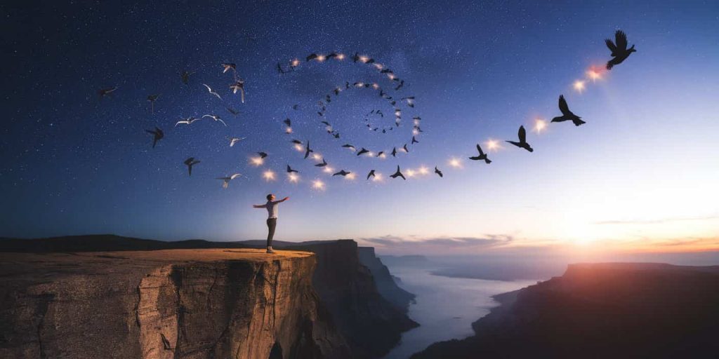 A person on a cliff with outstretched arms, surrounded by spiraling birds leaving trails of light against a night sky transitioning to sunrise, representing spiritual guidance and transformation.